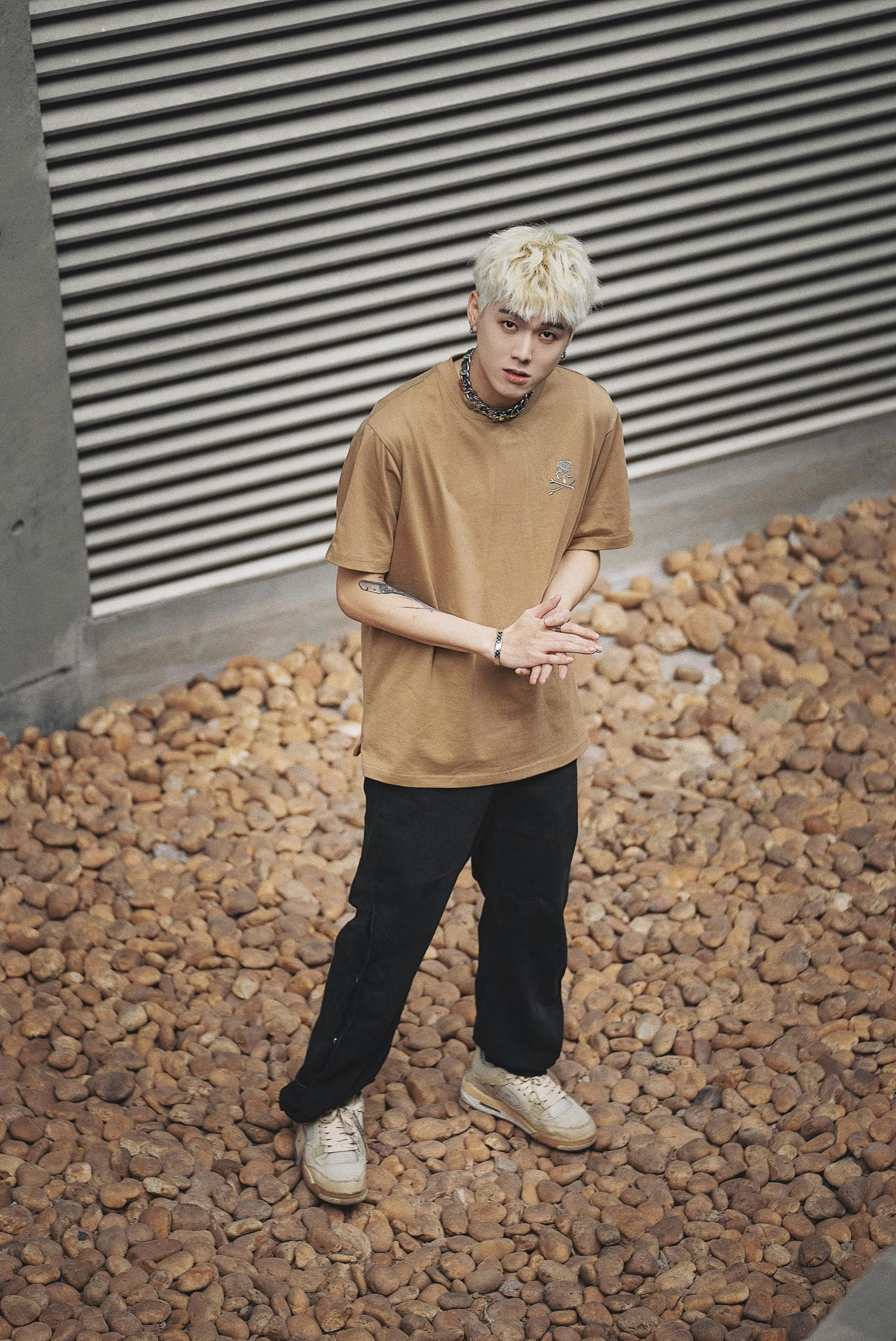 Stylish young man in casual attire poses expressively against a textured stone background.